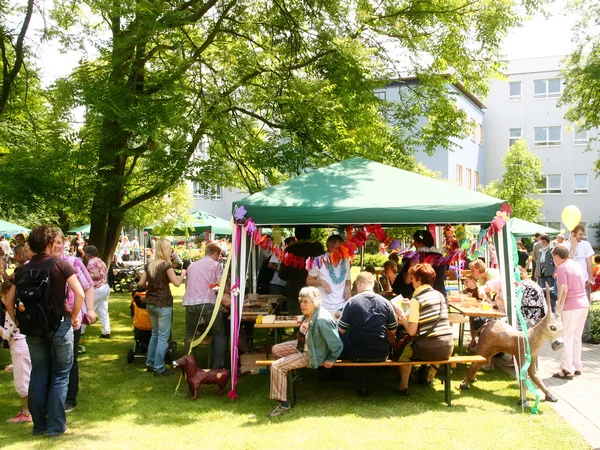 Menschen feiern fröhlich unter grünen Pavillons im Freien bei sonnigem Wetter.