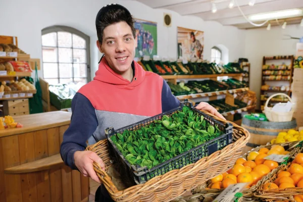 Junger Mann mit einem Korb Feldsalat im Hofladen des Klosterberghofs