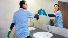 Reinigungskraft putzt einen Spiegel