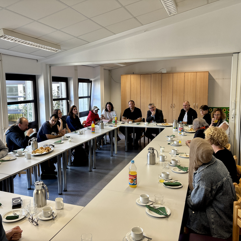 Menschen sitzen an Tischen in einem Raum und unterhalten sich bei Getränken und Snacks.