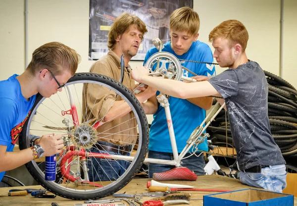 Lehrer zeigt Schülern, wie sie mit Werkzeug ein Fahrrad reparieren können.