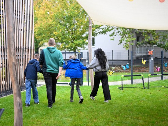 Zwei Jungs gehen Hand in Hand mit zwei Betreuern durch den Garten der Auszeit Bochum