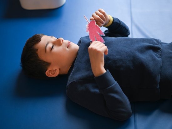 Ein kleiner Junge mit rotem Herbstlaub in den Händen entspannt sich im Liegen