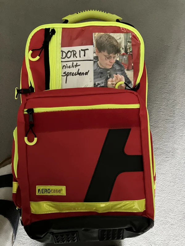 Roter Erste-Hilfe-Rucksack mit Fotoeinsatz und gelben Details.