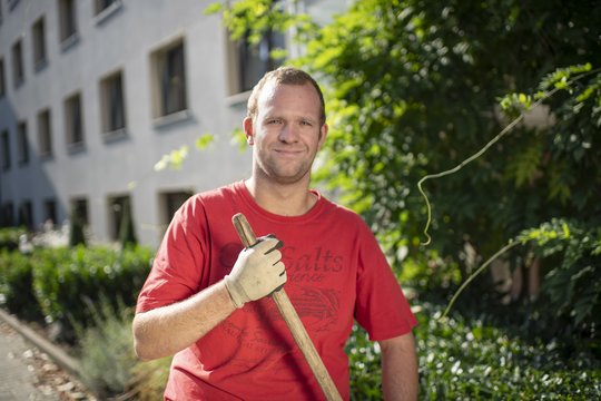 Beschäftigter aus dem Garten- und Landschaftsbau pflegt den Garten eines Kunden.