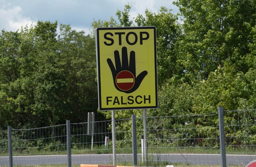 Verkehrsschild, auf dem eine Hand mit einem "Einfahrt-Verboten"-Symbol und den Worten "Stop Falsch" abgebildet ist. Bild: Canva