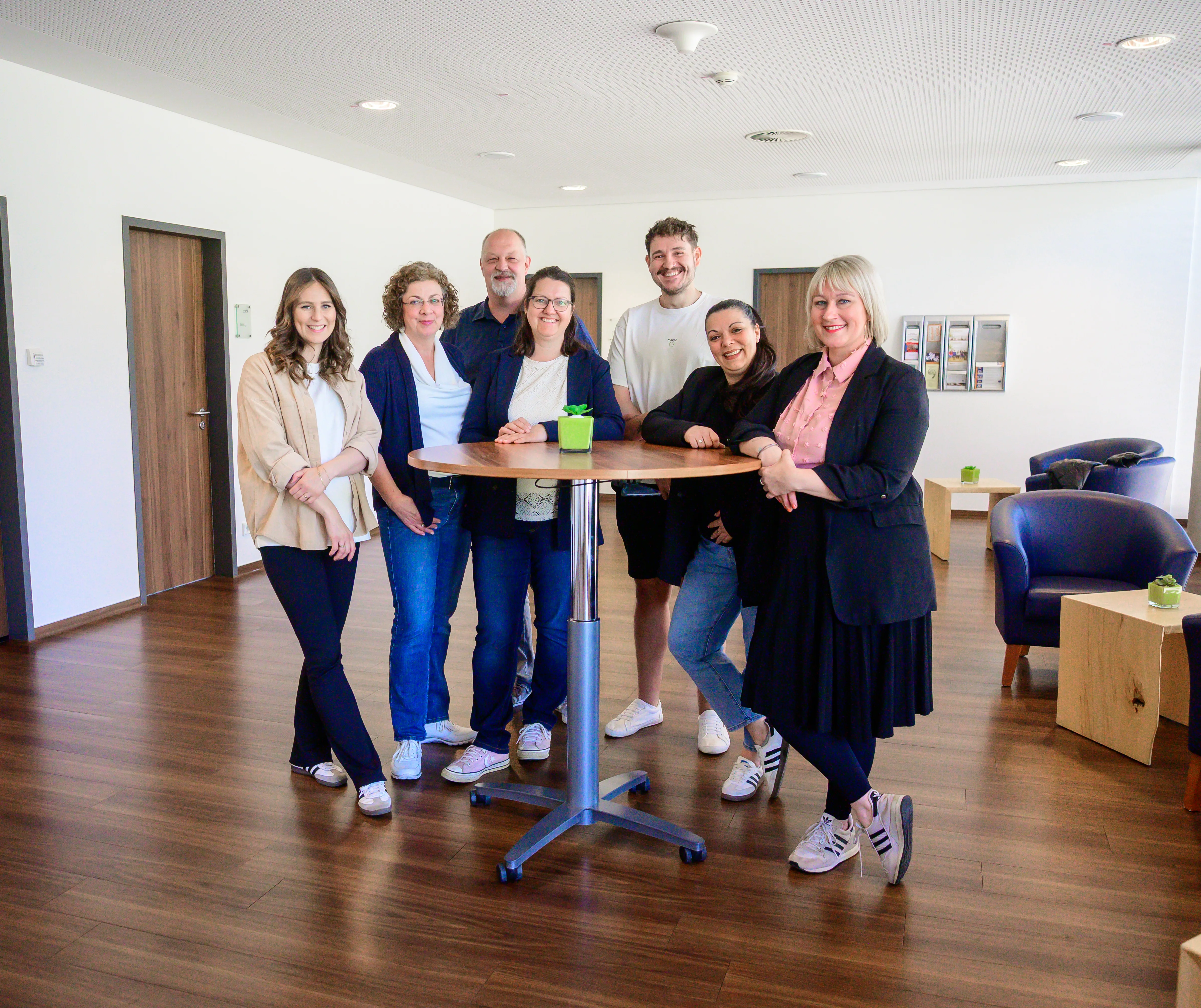 Mitarbeitende eines Bildungsträgers stehen gemeinsam um einen Stehtisch in einem offenen, freundlichen Pausenraum – symbolisch für Teamgeist und persönliche Entwicklung.